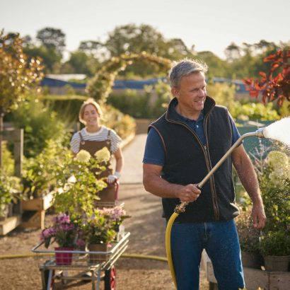 Mature Man And Woman Working Outdoors In Garden Centre Watering Plants