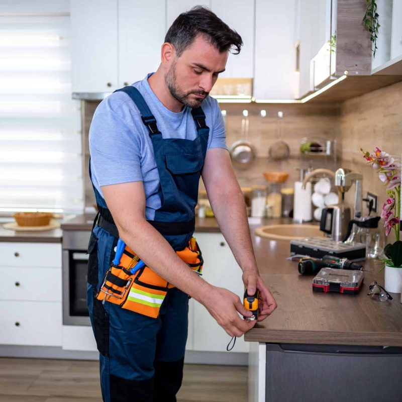 A worker focuses on repairs in a bright kitchen, surrounded by tools and equipment.