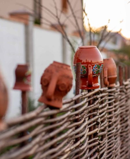 Beautiful handcrafted romanian ceramic pots and jugs are decorating a traditional wicker fence in the countryside during a warm sunset, showcasing the beauty of romanian rural life